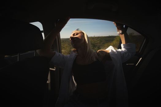 A beautiful girl rides in a car at speed and enjoys the wind from the window, rest from work and bustle, serenity and freedom. High quality photo