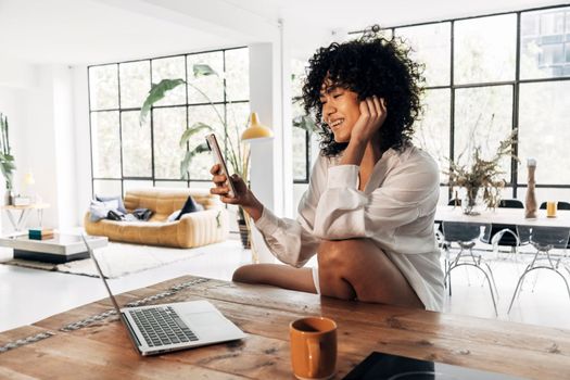 Young beautiful smiling african american woman video calling a friend in a bright beautiful loft apartment in the morning. Home concept. Technology concept.