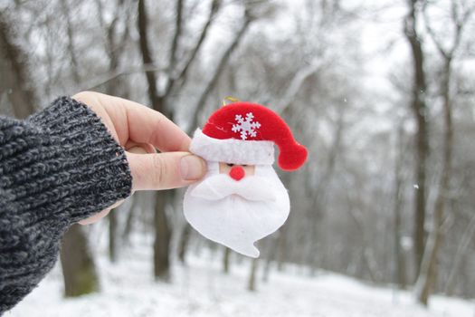 Merry Christmas concept. Male Hand holds Santa Claus on the background of the winter forest. Christmas background.