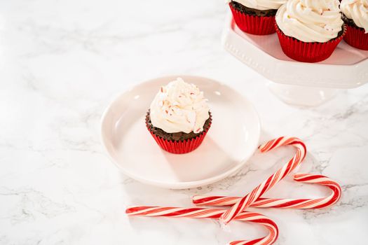 Freshly baked chocolate cupcakes with peppermint frosting and decorating with crushed peppermint candy cane candies.