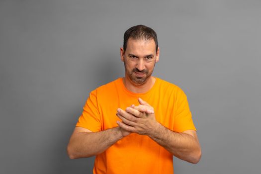 Cunning hispanic man rubbing his hands on isolated gray background, person rubbing his hands planning something, evil concept