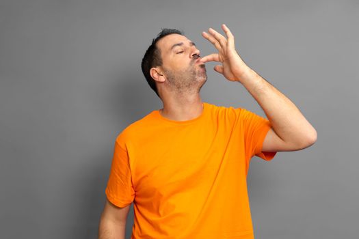Happy man licking fingers isolated on trendy gray studio background. Beautiful male half-length portrait. Satisfied man. Human emotions, facial expression concept. Front view