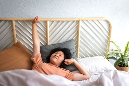 Young Asian woman waking up in the morning stretching arms in bed. Good morning. Lifestyle concept.