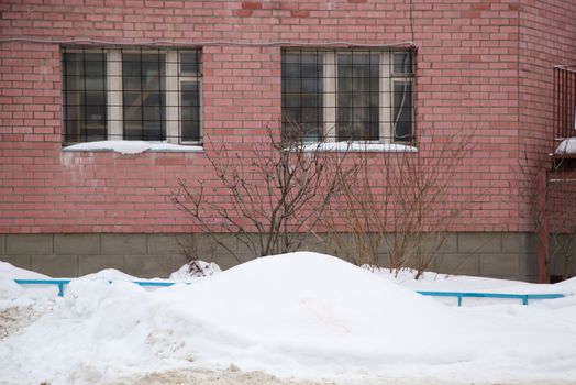 A small snowdrift on the background of the brick wall of the building. On the road lies white snow in high heaps. Urban winter landscape. Cloudy winter day, soft light.