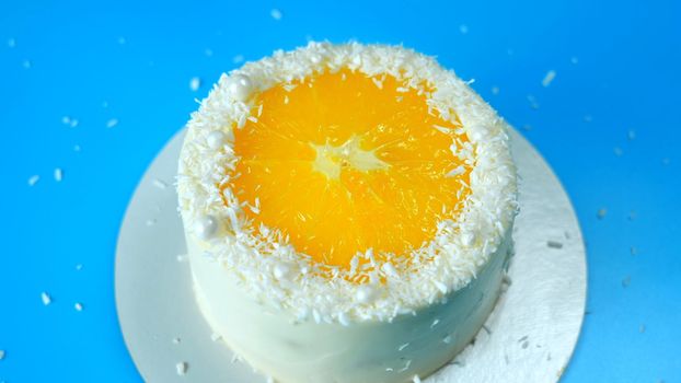 Cake with orange and coconut shavings spinning on a blue background