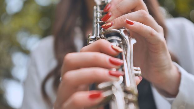 A girl plays the clarinet in the summer in the park. Close-up of her hands