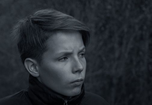 Dramatic black and white close-up portrait of a 13-year-old boy. A teenager with a concerned and serious look. High quality photo