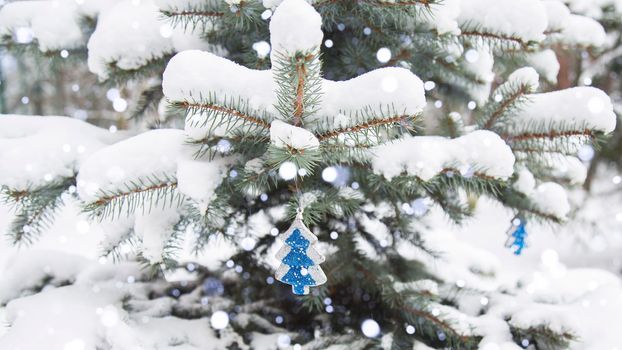 Winter, festive, New Year landscape. Snow is lying on the branches of a fir tree. Snowfall. Falling snow. Christmas tree toy to lead on the branch of the Christmas tree.