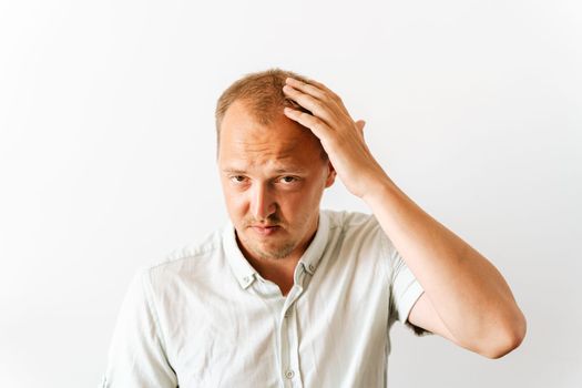 Before hair transplantation. Young sad bald man with depression at hair loss problems looking angry and frustrated and holding his head.