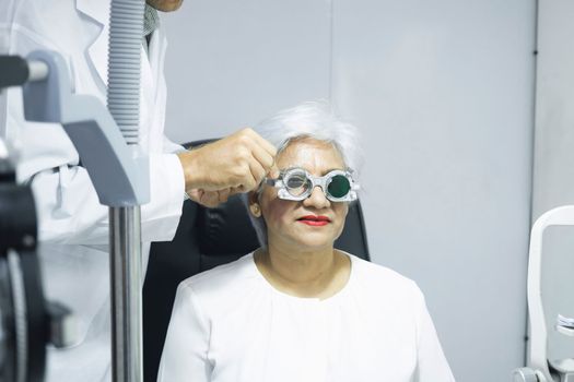 Woman sitting in optometrist cabinet having his eyesight checking, examining, testing with trial frame glasses by professional optician for new pairs of eyeglasses.