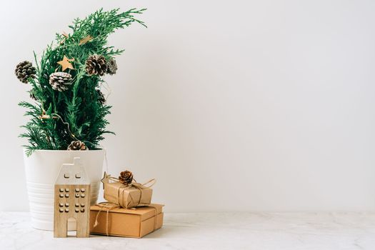 Creative natural miniature Christmas tree in pot on wooden table with gift boxes and white background. Xmas greeting card with copy space. Happy New Year