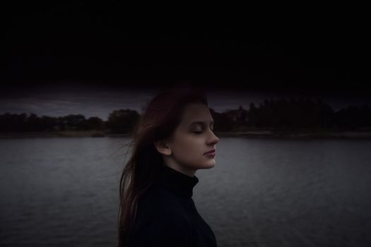 cute teenager girl closing her eyes enjoys the fresh air by the water in the evening outdoors. High quality photo