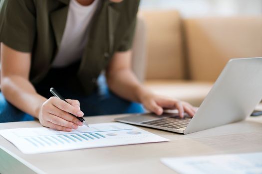 Close up of Young asian businesswoman working hard at the office using laptop data graphs, planning for improvement, analyzing and strategizing for business growth smiling at camera. Business concept.