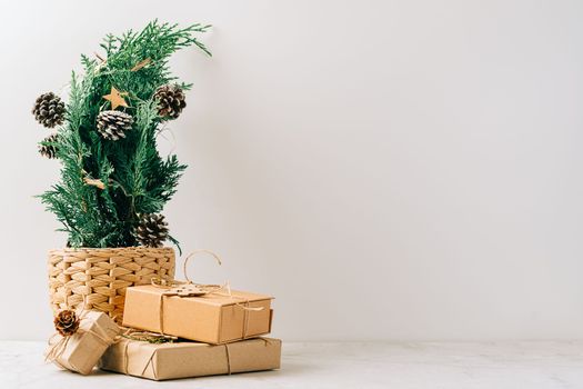 Creative natural miniature Christmas tree in pot on wooden table with gift boxes and white background. Xmas greeting card with copy space. Happy New Year