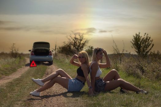 an accident on the road, a car broke down, two beautiful girl models are waiting for help. Car problem. Friends waiting for service. In the countryside . High quality photo