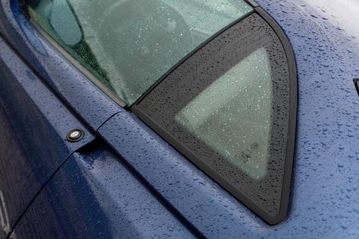 The body of a blue car covered with raindrops close up