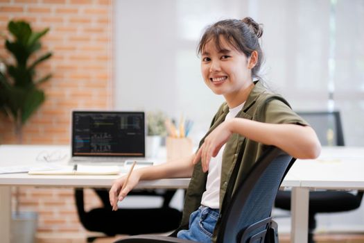 Close up of Young asian businesswoman working hard at the office using laptop data graphs, planning for improvement, analyzing and strategizing for business growth smiling at camera. Business concept.