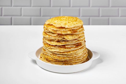 Stack of freshly baked pancakes lie in white ceramic form. Pancake week. Russian kitchen. Selective focus.