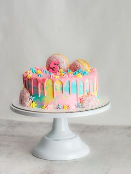 Close up of pink frosted dripping cake with donut and plastel brushed royal star sprinkles insolated on white studio shot