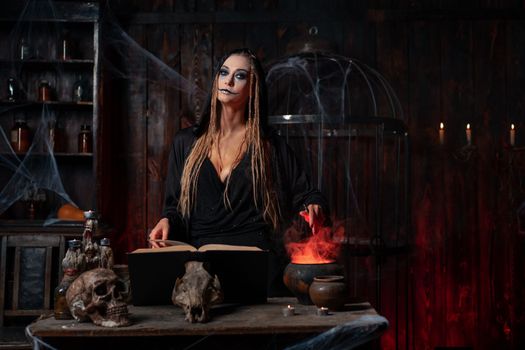 Witch use magic book and cauldron prepare poison or love potion. Black magic occult female wizard in dark room cage spider web human skull. Necromancer cooking magic potion. voodoo magic