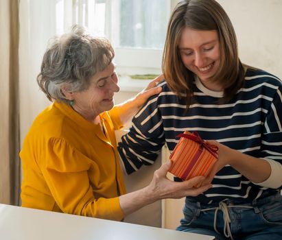 Two women, relatives, happily spend time together, grandmother and daughter give gifts to each other for the holidays, make pleasant surprises, love and emotional bonding inside the family.