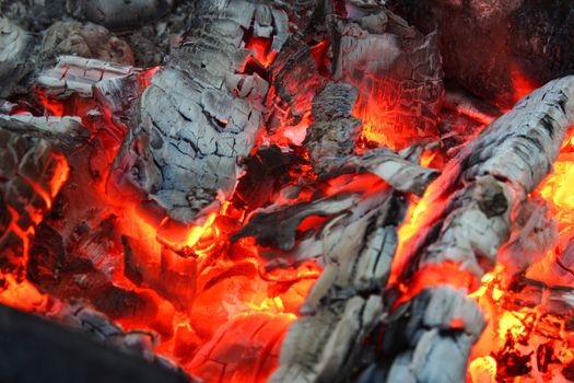 Smoldered logs burned in vivid fire close up. Atmospheric background with flame of campfire. Unimaginable detailed image of bonfire from inside with copy space. Whirlwind of smoke and glowing embers.