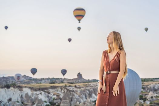 Tourist woman looking at hot air balloons in Cappadocia, Turkey. Happy Travel in Turkey concept. Woman on a mountain top enjoying wonderful view.
