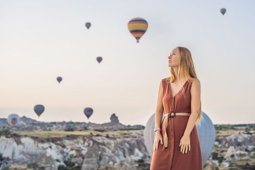 Tourist woman looking at hot air balloons in Cappadocia, Turkey. Happy Travel in Turkey concept. Woman on a mountain top enjoying wonderful view.