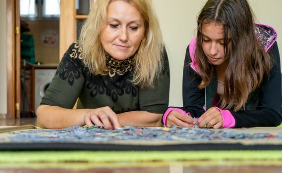 Mother and daughter lying on the floor doing a puzzle together while having a nice time on a girls night out.