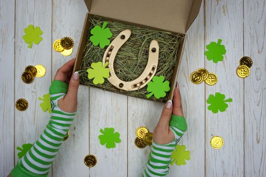 Women's hands hold a box with a gift for St. Patrick's Day. Horseshoe in a craft box filled with fresh hay. Background.