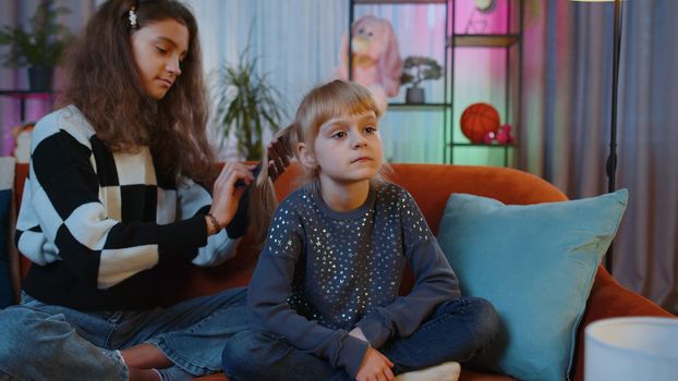 Teenage and little sisters child kids using combs brushing make hairstyle coiffure. Female siblings children or best friends combing long hair at home play room. Friendship family relationship concept