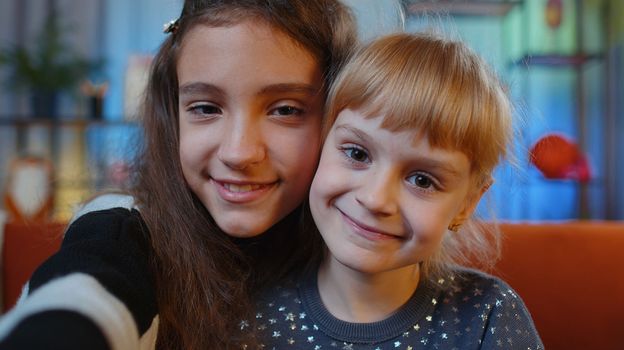 POV portrait of happy calm teenage and little sisters child kids smiling friendly, glad expression looking away dreaming resting, relaxation. Female siblings children or best friends at home playroom