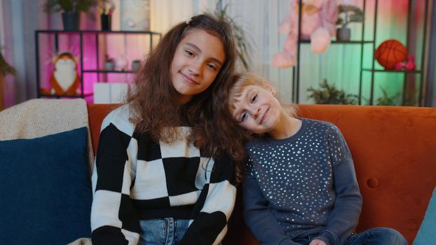 Portrait of happy smiling teenage child and little sister kid looking at camera. Female siblings children or best friends sitting on sofa at home play room. Friendship, family relationship concept
