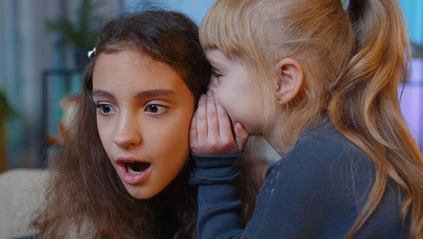 Teenage child whisper news rumors in ear to little sister kid girl share telling secrets gossip having fun. Female siblings children or best friends at home play room. Friendship, people communication