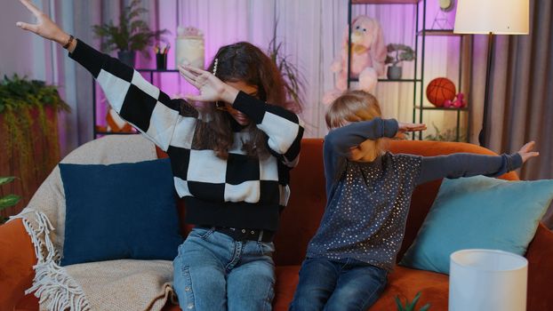 Teenage child and little sister kid girls wearing stylish sunglasses listening music and dancing disco fooling around having fun, relaxing on party. Siblings children or best friends at home play room