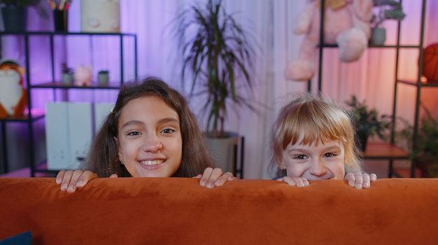 Teenage child and little sister kid girls playing hide and seek peekaboo game. Female smiling siblings children or best friends trying to scare, prank at home play room. Friendship family relationship