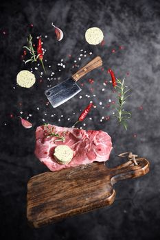 Art photo levitation of a meat steak with ingredients for frying oil spices rosemary pepper garlic on a gray background. High quality photo