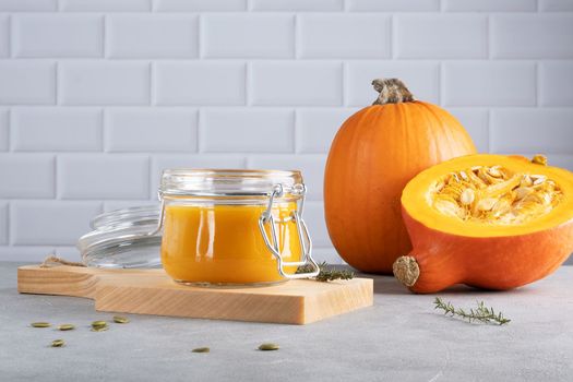 Pumpkin puree soup with pumpkin seeds and thyme in a glass jar on a wooden kitchen board. Ripe pumpkin. Healthy diet. Selective focus.