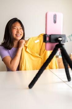 Asian female fashion influencer recording video for social media showing clothes to followers. Vertical.Technology.