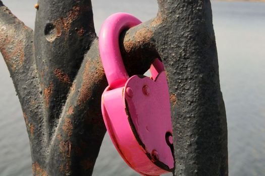 A pink lock in the shape of a heart close-up hangs on a rusty lattice. wedding tradition. The concept of love and fidelity.