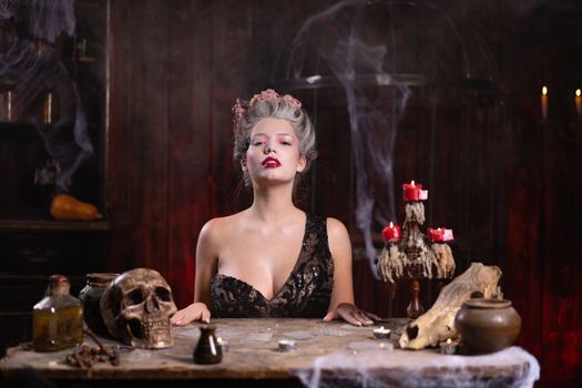 Portrait fortune teller woman reading future on magical cards. Magic and divination. Young beautiful enchanted female witch sitting on the table waiting your desire. Scary