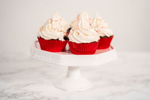 Freshly baked chocolate cupcakes with peppermint frosting and decorating with crushed peppermint candy cane candies.