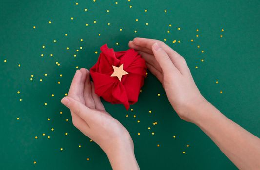 Woman hands holding paper free gift wrapping technique Furoshiki. Viva magenta on dark teal background. Flat lay, hands and present box, top view. Christmas, valentines and birthday concept