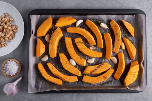 Pieces of ripe pumpkin prepared for baking in the oven. Pumpkin on a baking sheet with olive oil, garlic and dry thyme on the kitchen table. Healthy food. View from above. Selective focus.