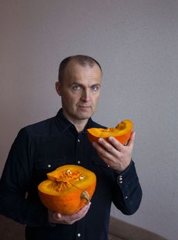 A nice positive man in a blue shirt holds two large pieces of pumpkin in his hands.