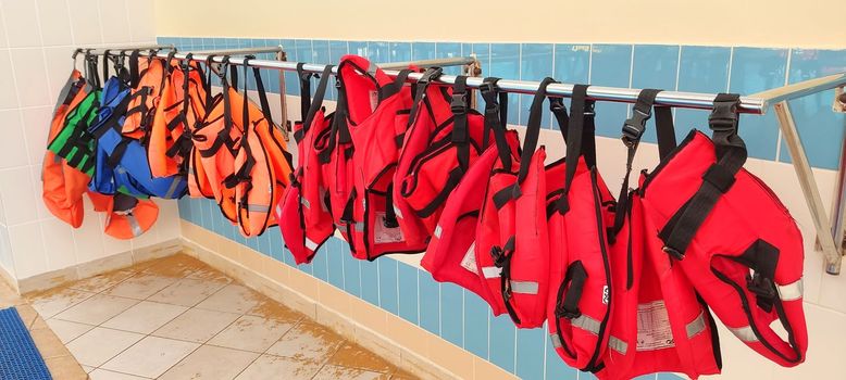 Several red and orange life jackets hang on a hanger, near the gouboi tile wall in the pool.