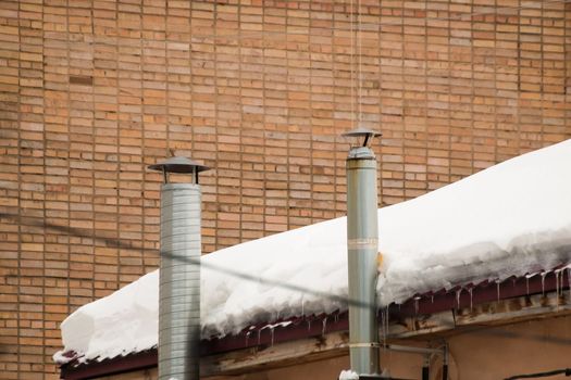 Metal exhaust ventilation pipes on the background of a brick wall. Roof of the house in the snow. Cloudy, cold winter day, soft light.