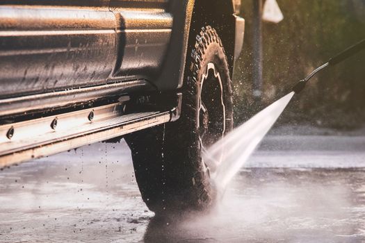Washing offroader car at a self-service car wash with a high-pressure water jet after off-road driving.