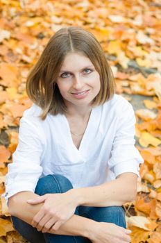 Portrait of a beautiful caucasian girl sitting on falling yellow leaves and smiling, autumn leaf fall, High quality photo