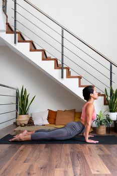 Asian female yogi doing upward facing dog yoga pose at home living room. Vertical image. Wellness and healthy lifestyle concept.